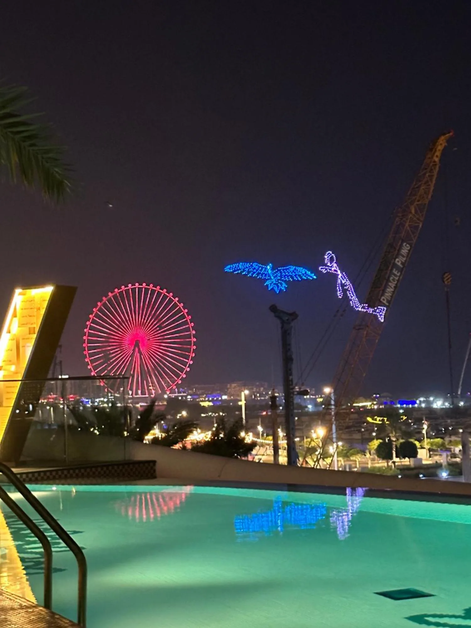 Vista nocturna de la piscina en Magic JBR & Dubai Marina en Dubai con la noria iluminada de Ain Dubai al fondo.