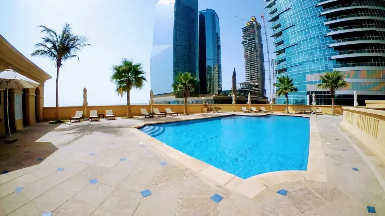 Terraza de la piscina exterior en Magic JBR & Dubai Marina en Dubai, rodeada de palmeras y torres de gran altura.