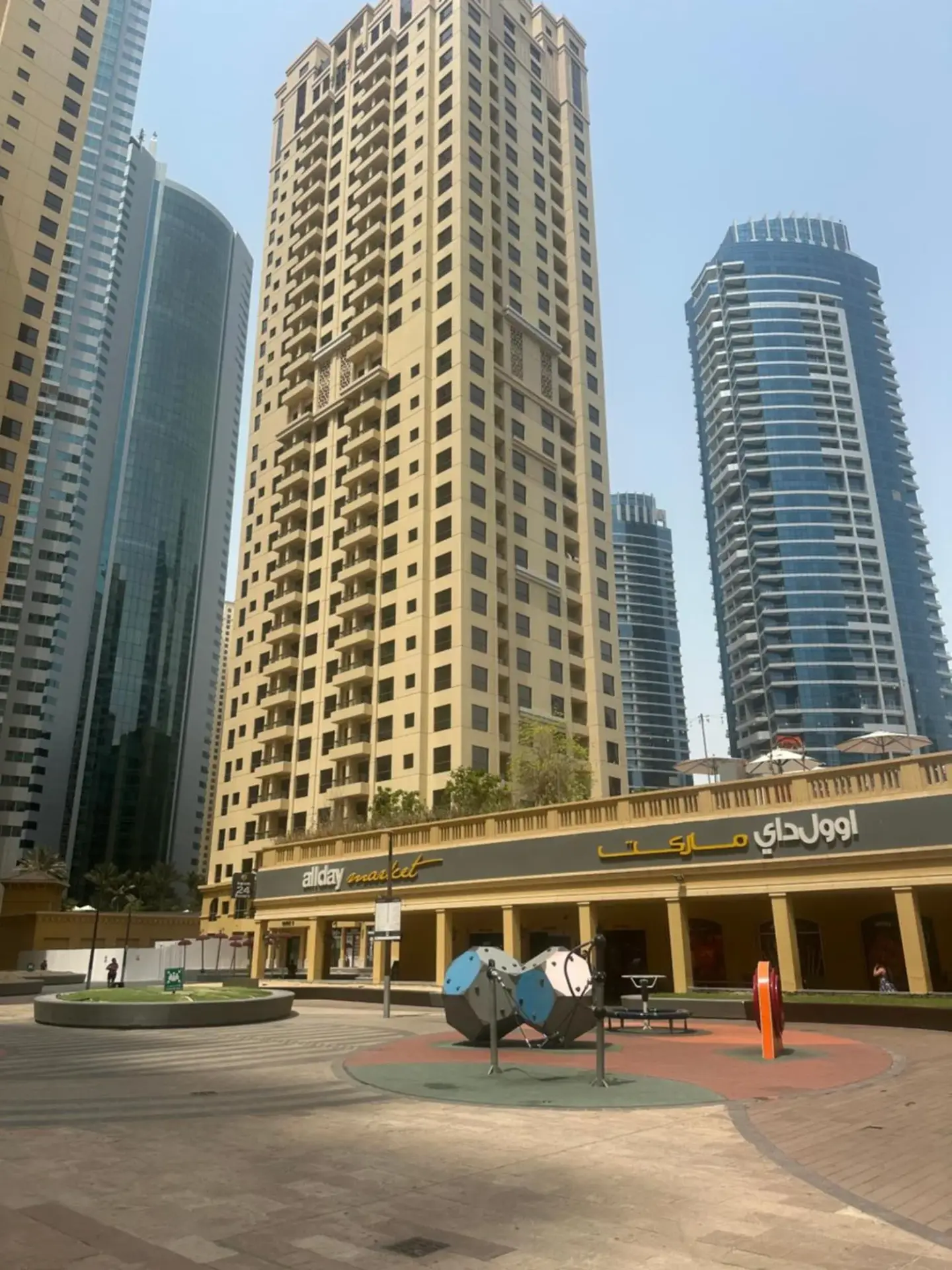 Plaza urbana cerca de Magic JBR & Dubai Marina en Dubai con altas torres residenciales y locales comerciales.
