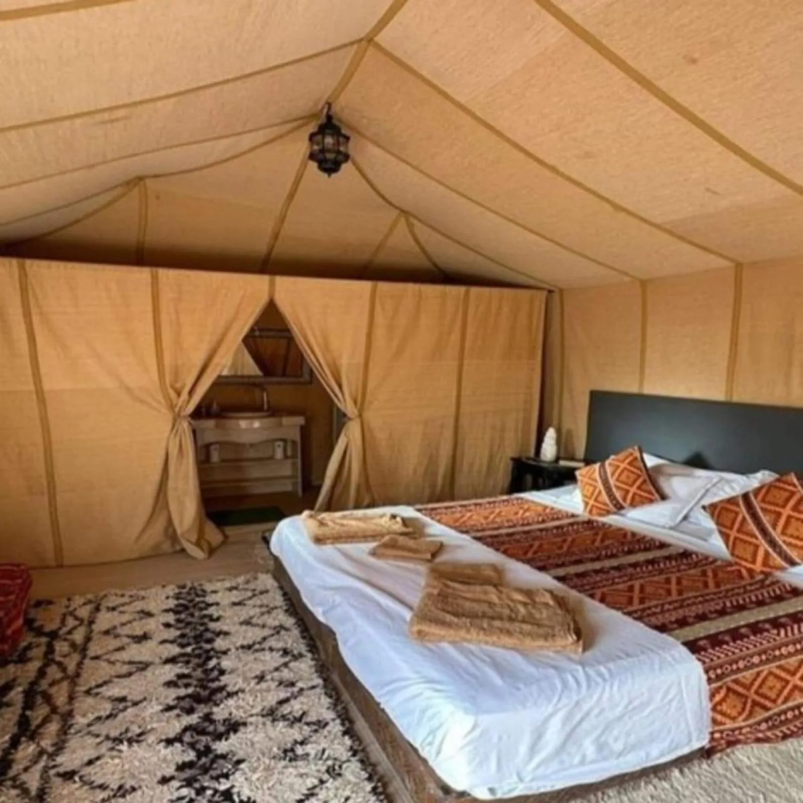Geräumiges Zeltzimmer im Magnifique Luxury Camp in Merzouga mit Kingsize-Bett, gemusterten Teppichen und privatem Waschbereich.