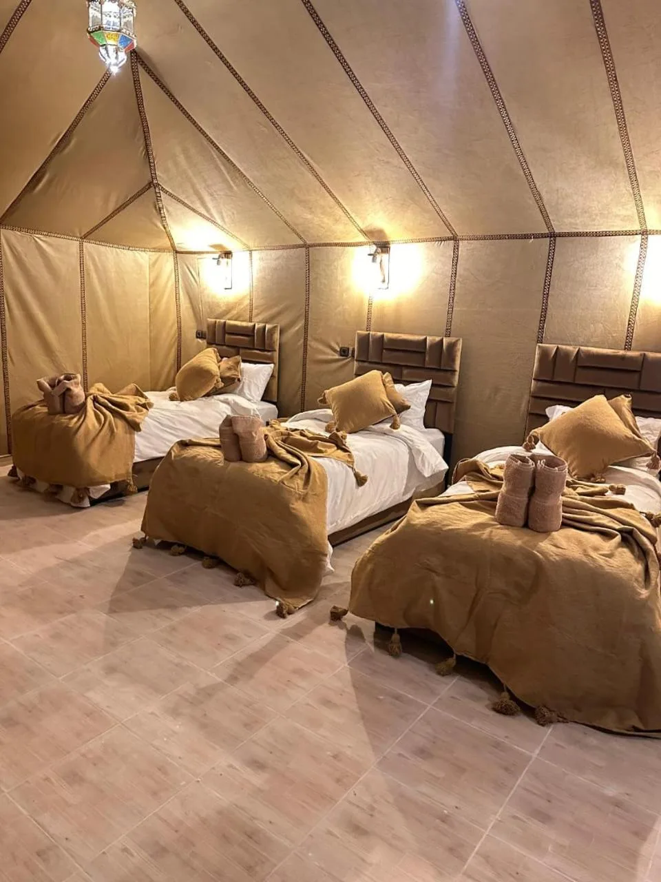 Dreibett-Zeltzimmer im Magnifique Luxury Camp in Merzouga mit drei Einzelbetten und warmer Bettwäsche im Wüstenstil.