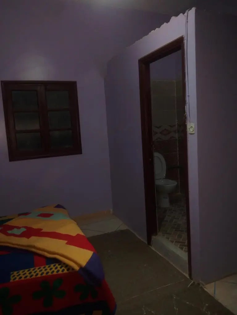Dimly lit bedroom at Maison La Baraka Merzouga in Merzouga with an en-suite bathroom visible through the open door.