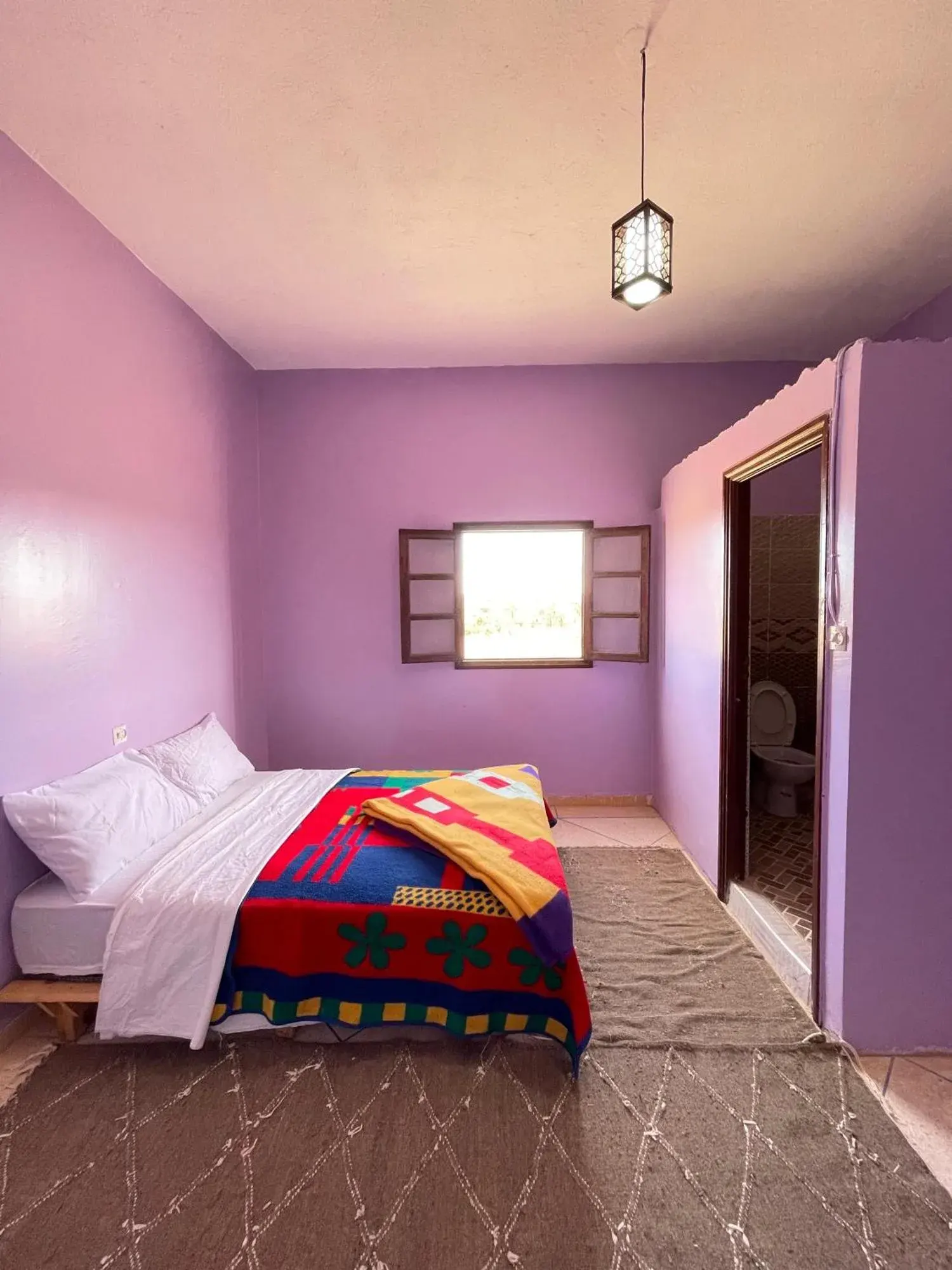 Double room at Maison La Baraka Merzouga in Merzouga with purple walls, a bed, rug, and an en-suite bathroom entrance.