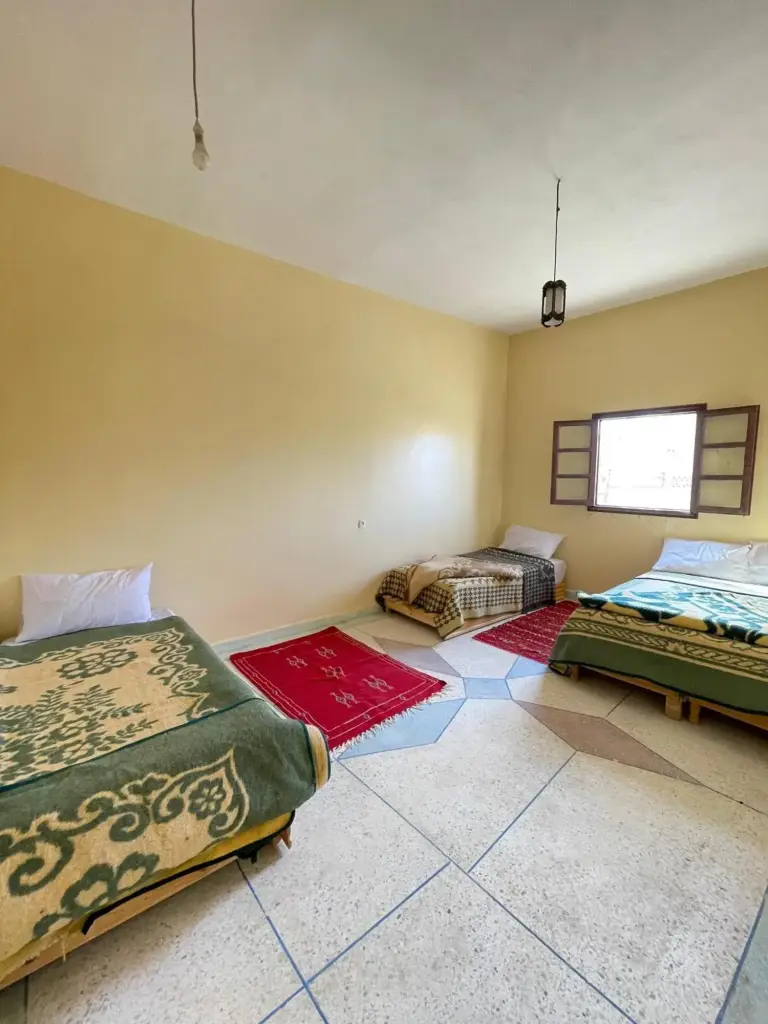 Shared room at Maison La Baraka Merzouga in Merzouga with three single beds, tiled floor, and window light.