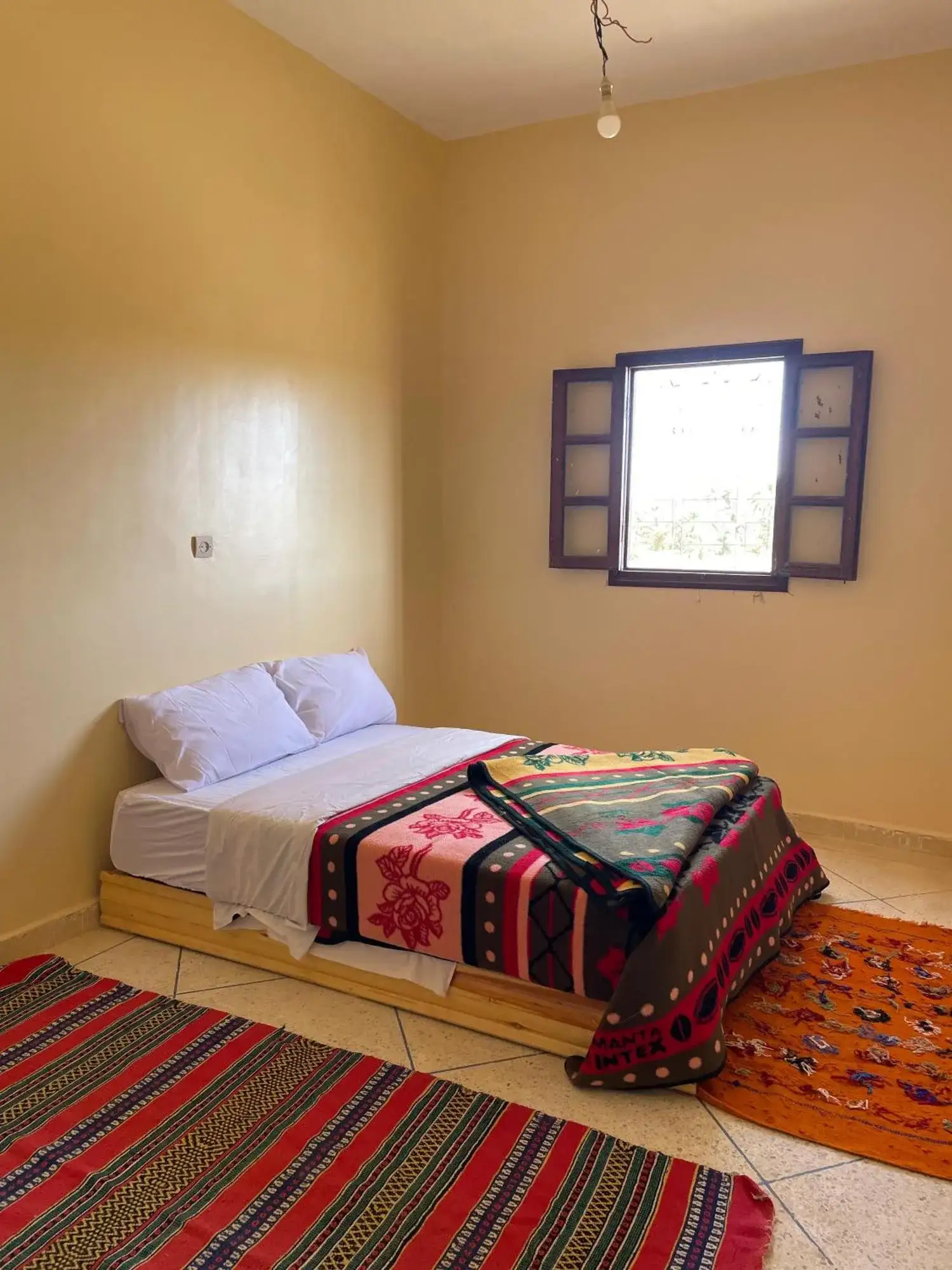 Single room at Maison La Baraka Merzouga in Merzouga with beige walls, a bed, and a window with shutters.