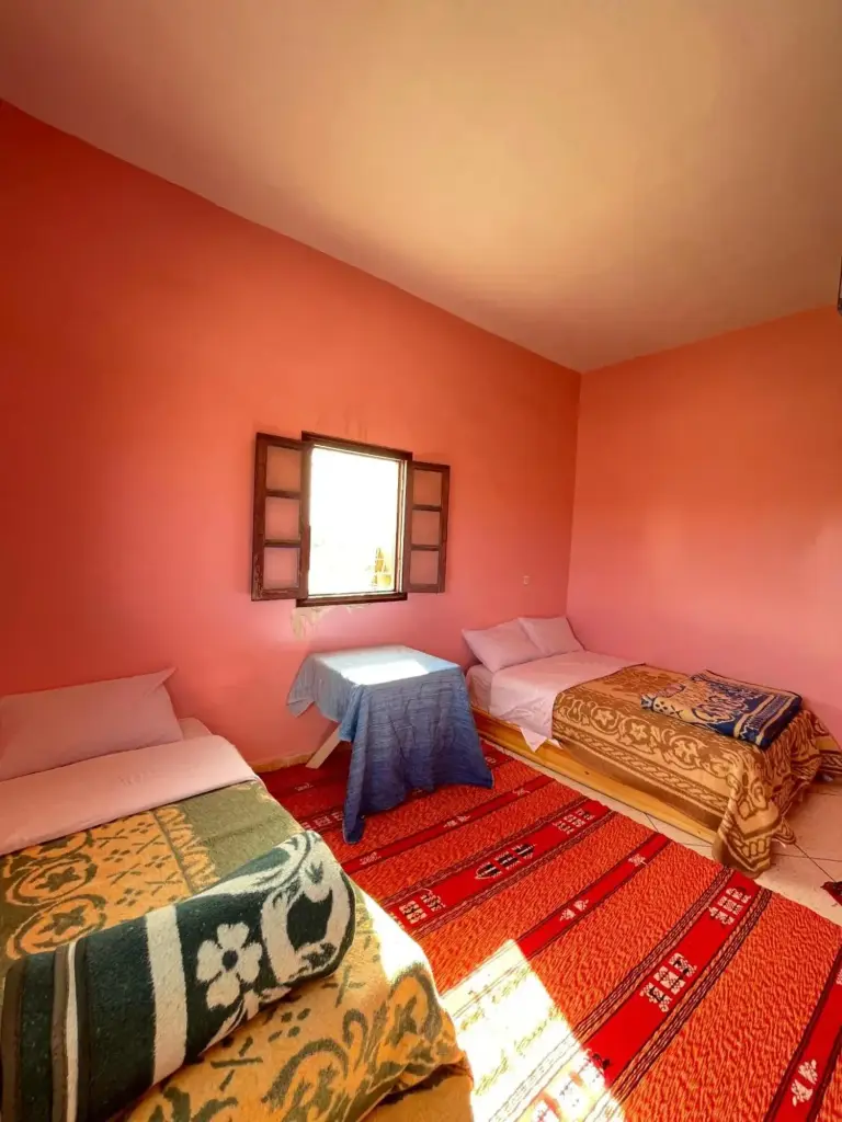 Triple room at Maison La Baraka Merzouga in Merzouga with pink walls, three beds, and a central table.