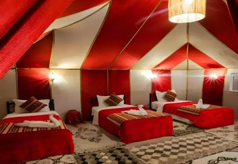 Majestic Dunes Luxury Camp – hotel en Merzouga, Marruecos – una habitación con tres camas en una tienda roja y blanca en Majestic Dunes Luxury Camp en Merzouga