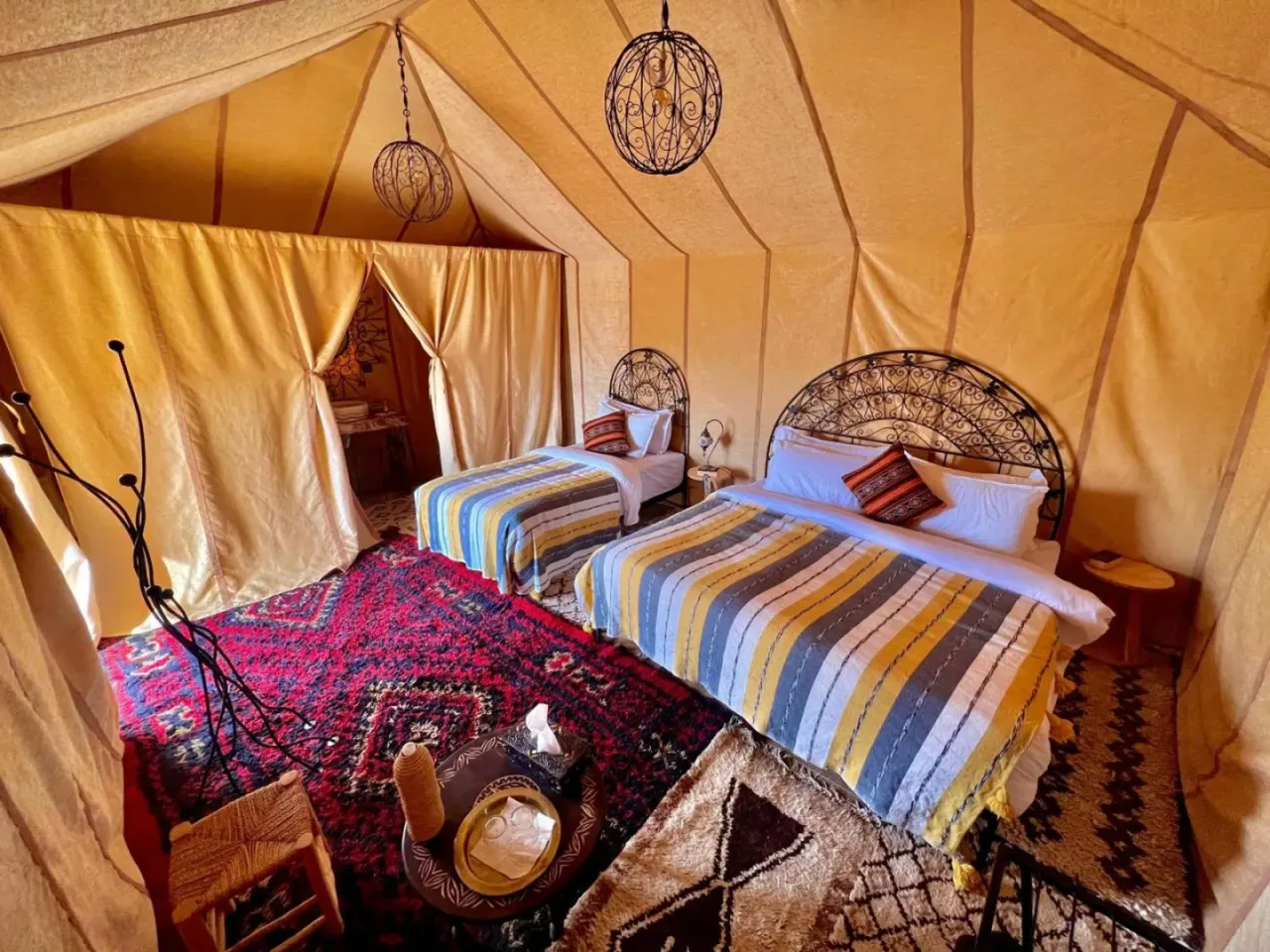 Chambre tente Triple à Maria'S Luxury Camp à Merzouga avec trois lits, un décor tressé et des tapis à motifs rouges