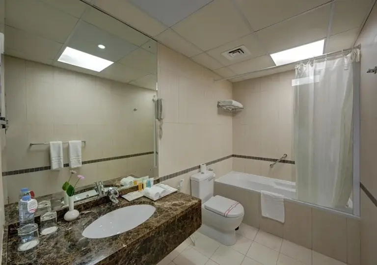 Marina Hotel Apartments Dubai bathroom with bathtub, shower curtain, marble vanity, and mirror