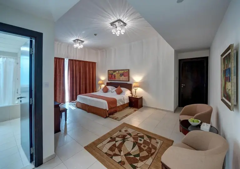 Marina Hotel Apartments Dubai studio bedroom with a king bed, seating area, and balcony curtains