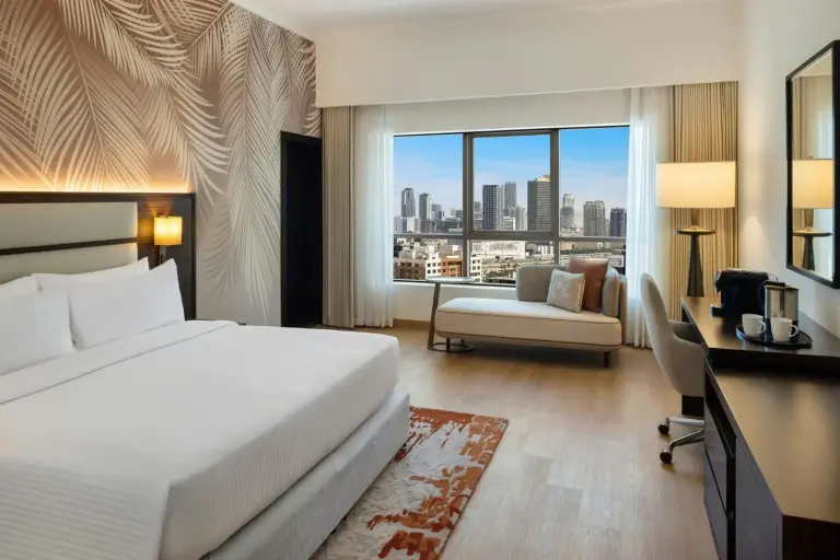 Geräumiges Gästezimmer im Marriott Hotel Production City, Dubai mit Kingsize-Bett, Fenster mit Stadtblick und Schreibtisch