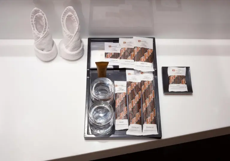 Gästeausstattung im Merlynn Park Hotel Jakarta mit Hausschuhen, Trinkgläsern und verpackten Pflegeprodukten.