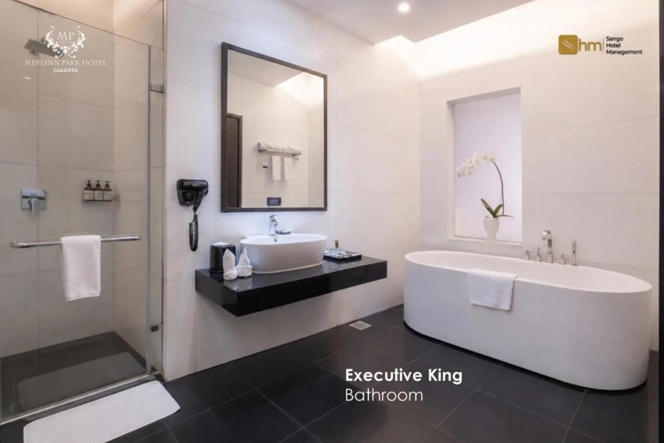 Executive King Badezimmer im Merlynn Park Hotel Jakarta mit Badewanne, Glasdusche und modernem Waschtisch.