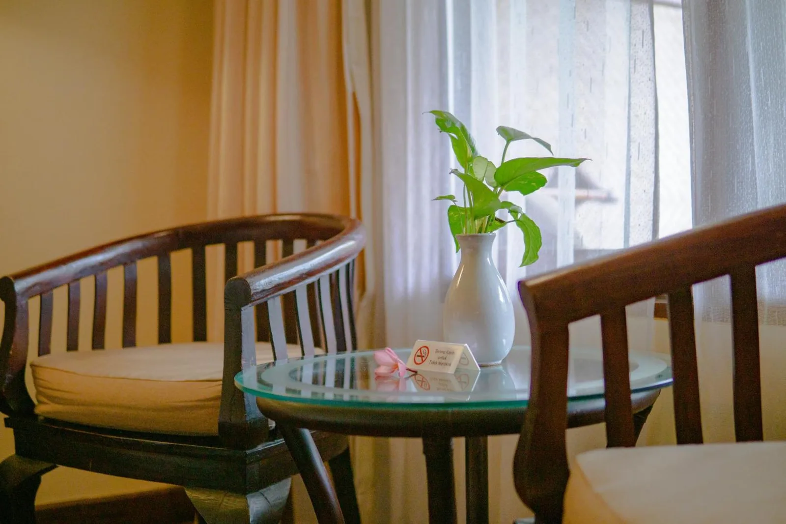 Sillas y mesa junto a la ventana en Merumatta Senggigi Lombok en Mataram con un pequeño jarrón
