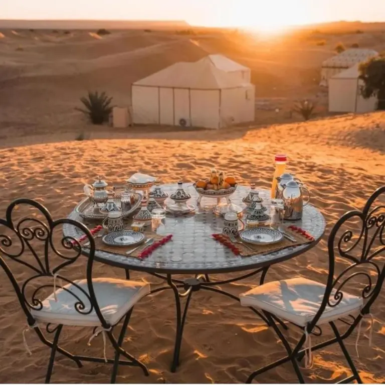 Mesa de té al aire libre en Merzouga Alicante Luxury Camp en Merzouga con el atardecer del desierto de fondo