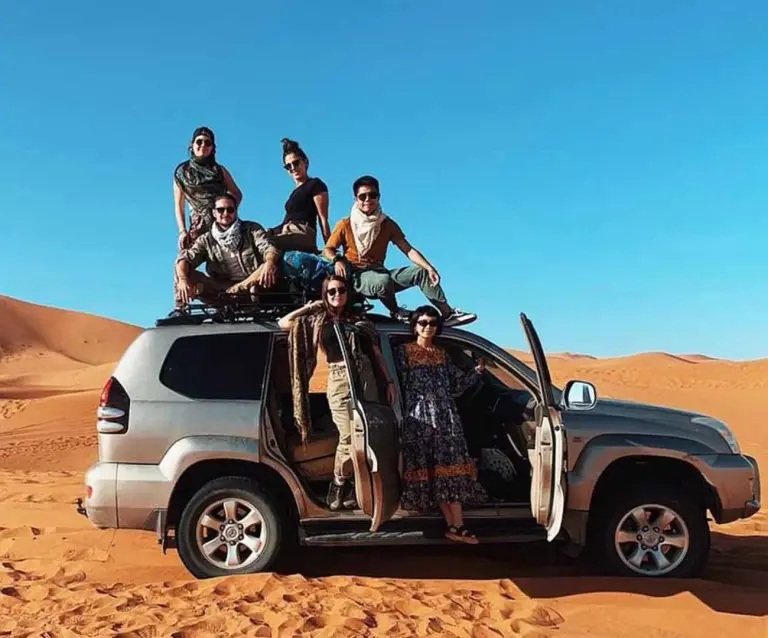 Gäste, die auf einem 4x4-Fahrzeug in der Sahara-Wüste nahe dem Merzouga Berber Camp in Merzouga posieren