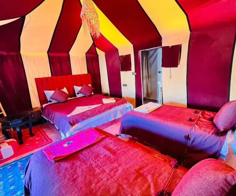 Vierbett-Zeltzimmer im Merzouga Berber Camp in Merzouga mit drei Betten, farbigen Berber-Zeltwänden und gemusterten Teppichen