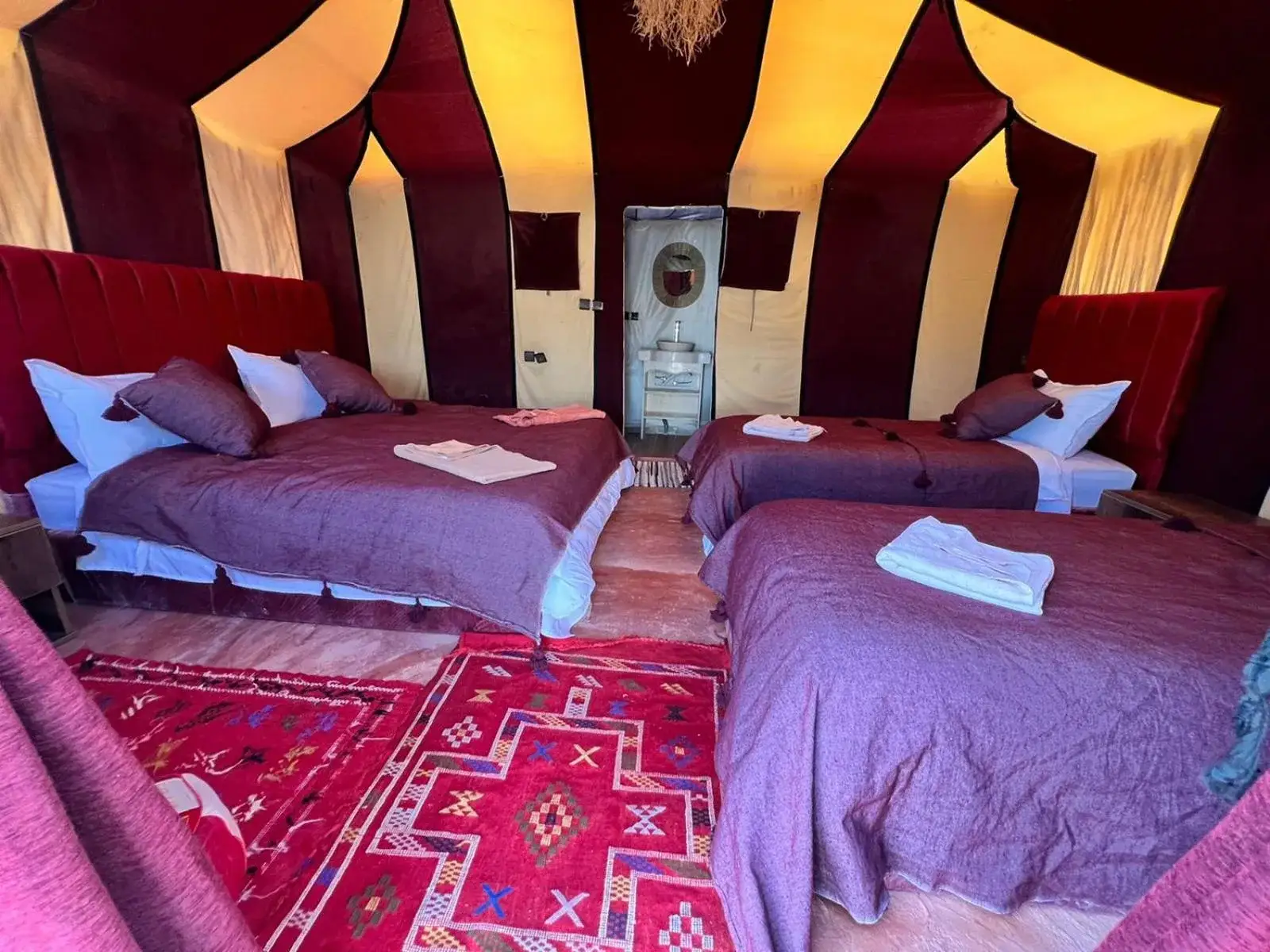 Dreibett-Zeltzimmer im Merzouga Berber Camp in Merzouga mit drei Betten, Berber-Dekor und einem Eingang zum privaten Badezimmer