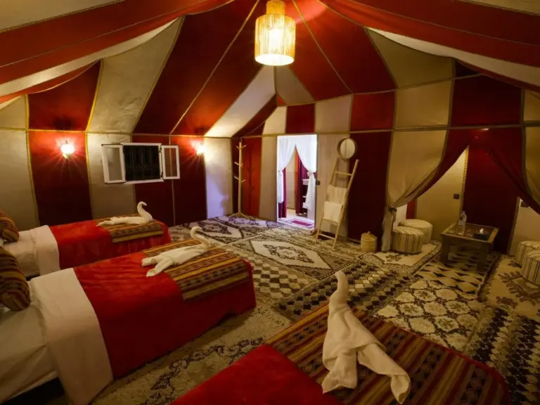 Suite en tienda de lujo en Merzouga DuneNova Luxury Camp en Merzouga con varias camas, alfombras estampadas y zona de estar en la tienda