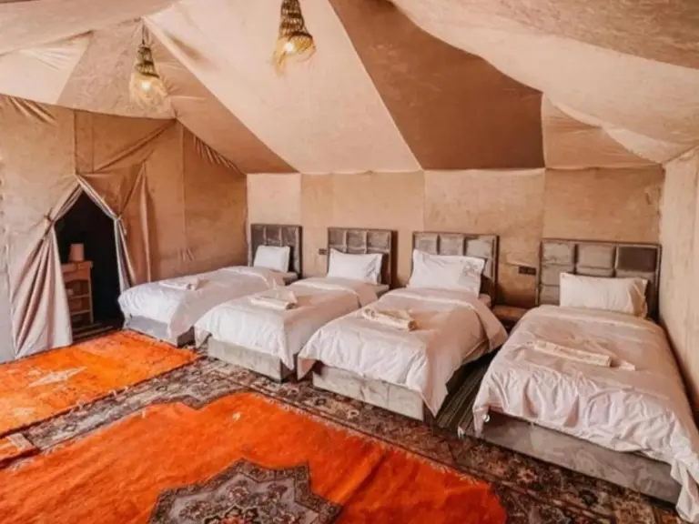 Habitación tienda cuádruple en Merzouga DuneNova Luxury Camp en Merzouga con cuatro camas individuales y alfombra naranja