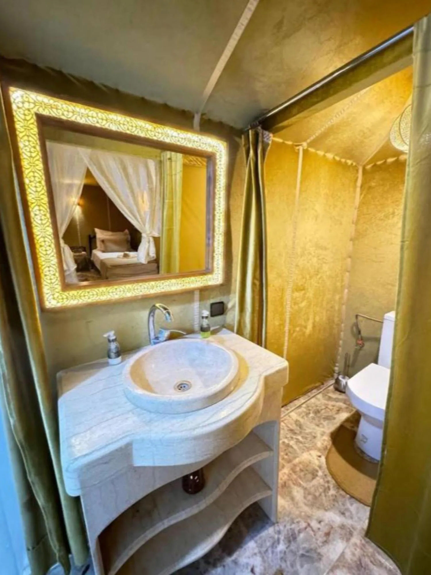 Interior del baño en Merzouga Eastern Camp Luxury en Merzouga con lavabo de piedra, espejo iluminado y zona de ducha.