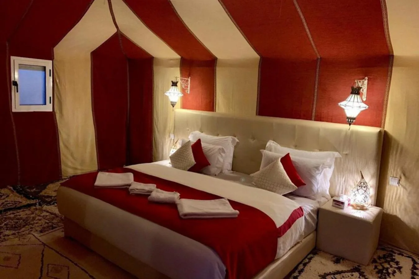 Suite con cama doble en Merzouga Eastern Camp Luxury en Merzouga con ropa de cama roja y elegante decoración de tienda.
