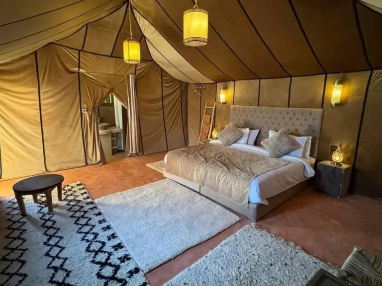 Habitación en tienda con cama king-size en Merzouga Eastern Camp Luxury en Merzouga con una cama grande, alfombra y acceso privado al baño.