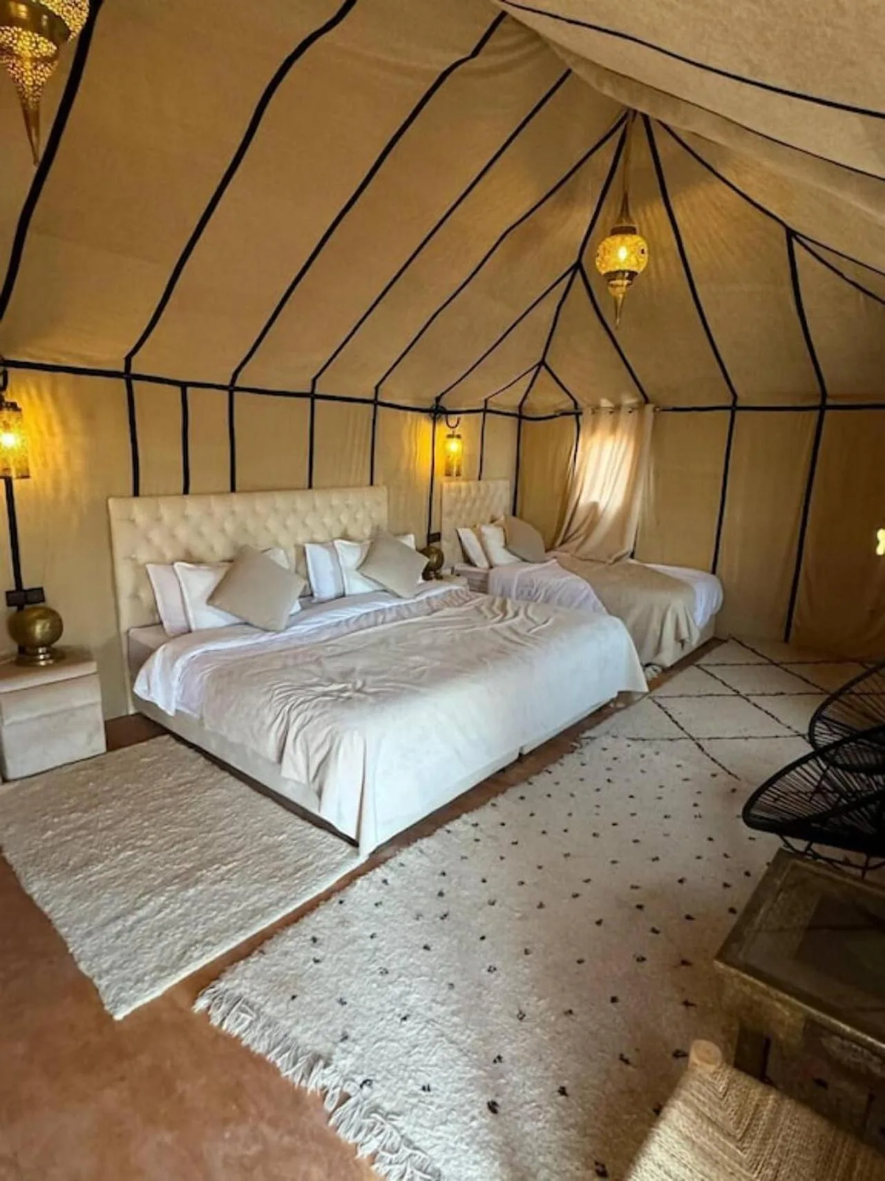 Dormitorio de tienda de lujo en Merzouga Eastern Camp Luxury en Merzouga con una cama grande, una cama individual y una decoración cálida de estilo desértico.