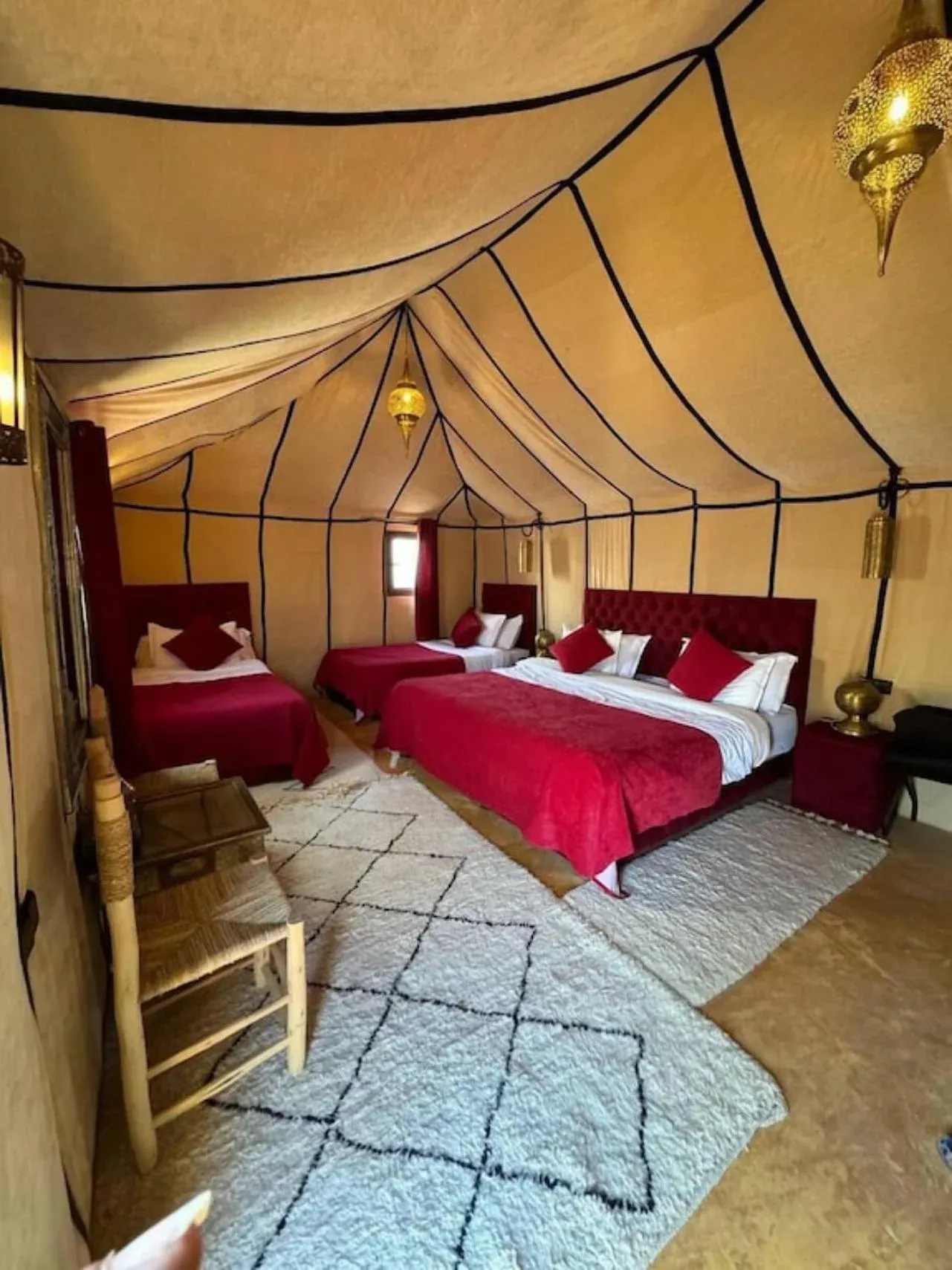 Suite de tienda de lujo de temática roja en Merzouga Eastern Camp Luxury en Merzouga con varias camas y alfombras estampadas.