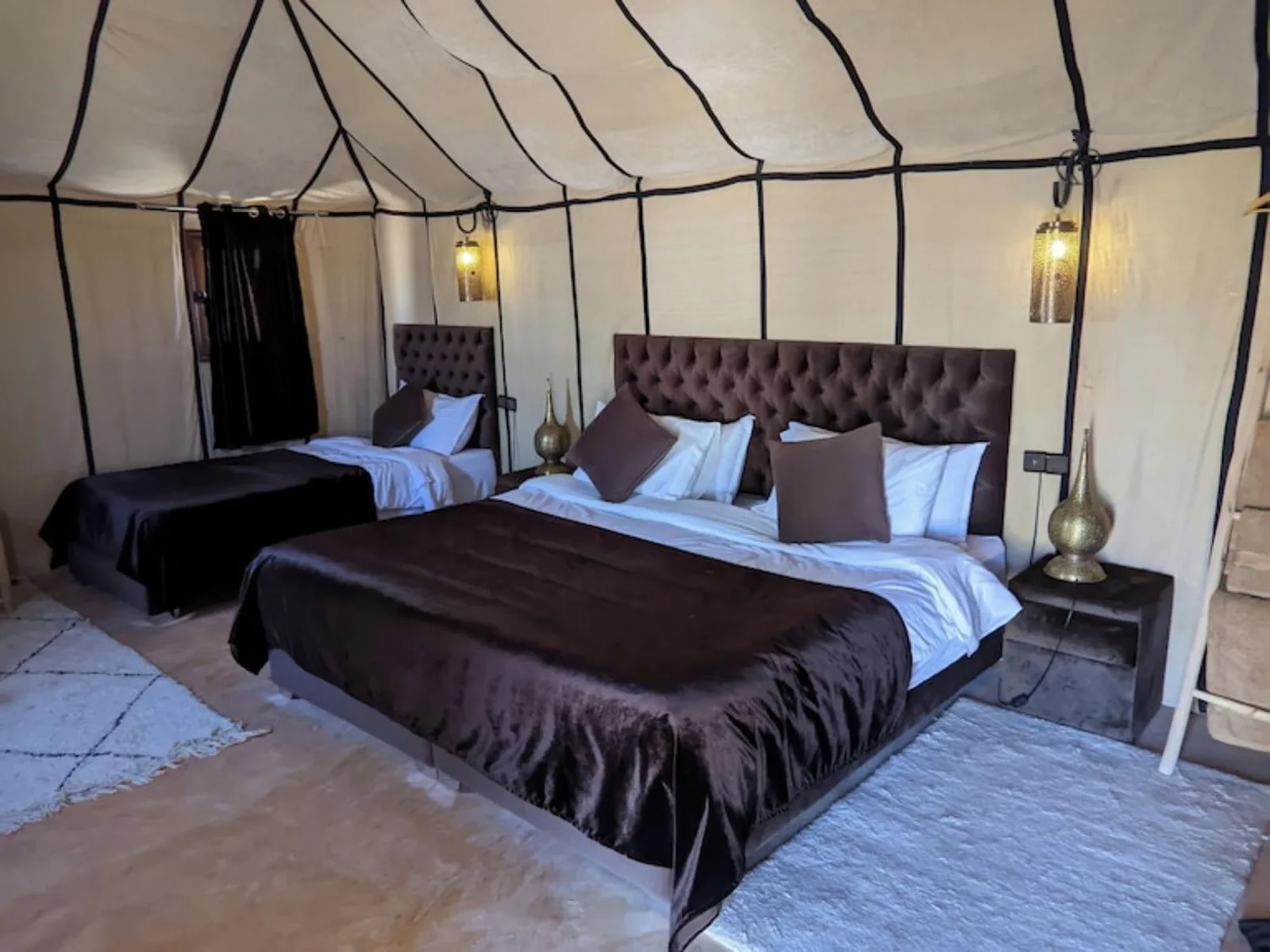 Tienda de lujo con dos camas en Merzouga Eastern Camp Luxury en Merzouga con ropa de cama oscura y suave iluminación de farolillos.