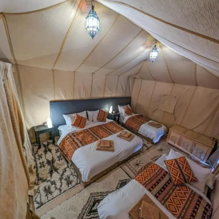 Triple tent room at Merzouga Golden Dunes Luxury Camp in Merzouga with three beds, patterned textiles, and cozy glamping decor.