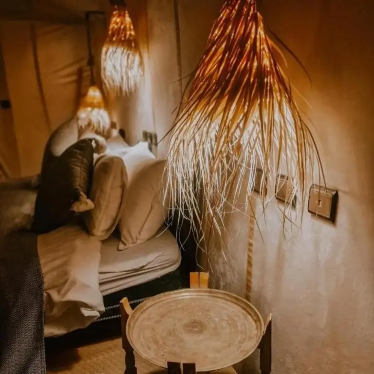 Gemütliche Bettnische im Merzouga Legacy Camp in Merzouga mit warmem Ambiente-Licht und geflochtenen Hängelampen