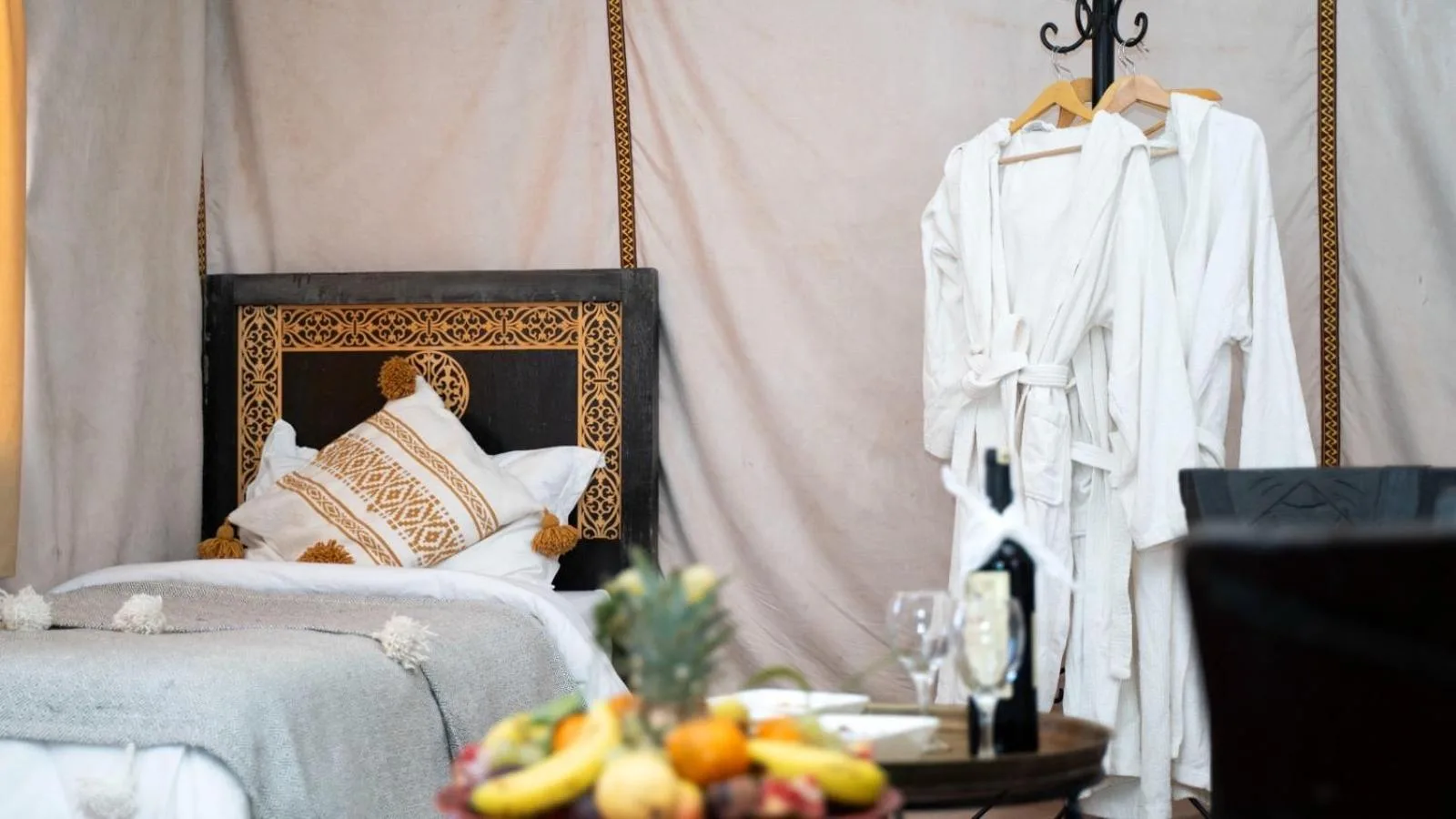Single bed corner with robes and fruit tray inside Merzouga Luxe Camp in Merzouga