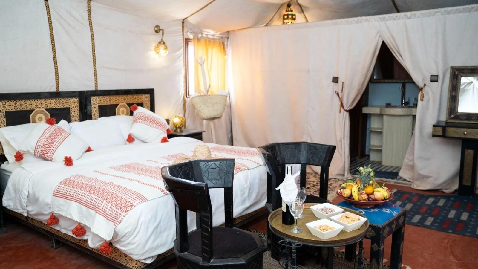 Elegant tent bedroom with bed, robes, and fruit service at Merzouga Luxe Camp in Merzouga