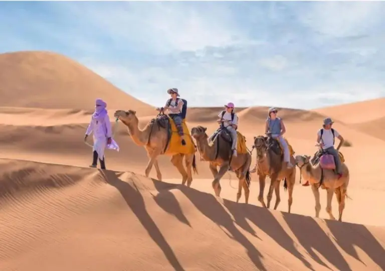 Touristen erkunden die Dünen auf dem Kamelrücken im Merzouga Luxe Desert Camp