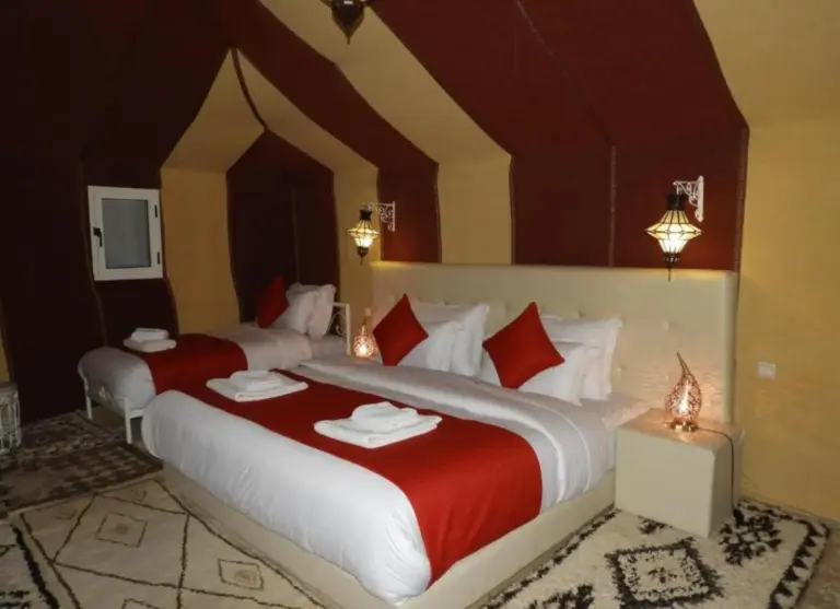 Habitación triple de Merzouga Luxurious Camp con ropa de cama roja y diseño de tienda marroquí en Merzouga, Marruecos