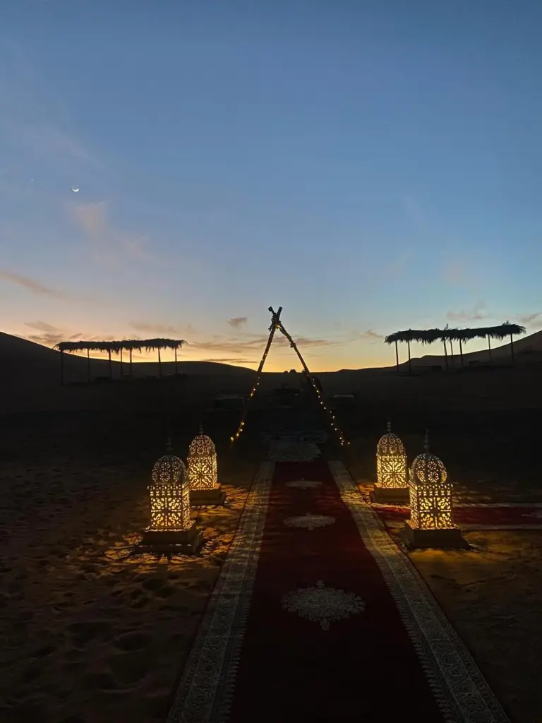 Camino de entrada iluminado con faroles en Merzouga Luxury Camping en Merzouga durante la puesta de sol en el desierto del Sáhara