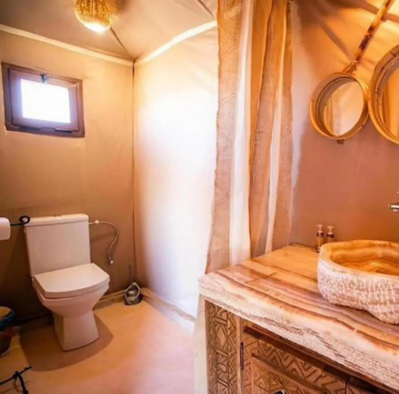Bathroom interior at Merzouga Retreat Camp in Merzouga with a toilet, sink, mirror, and shower curtain.