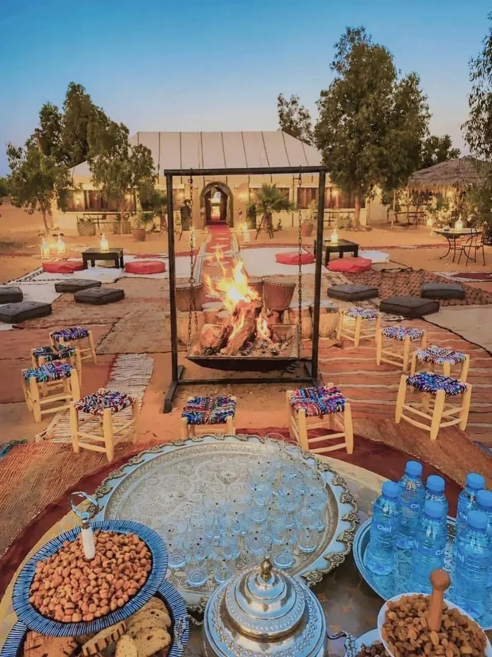 Exterior view of Merzouga Retreat Camp in Merzouga with a central fire pit, seating area, and desert camp courtyard.