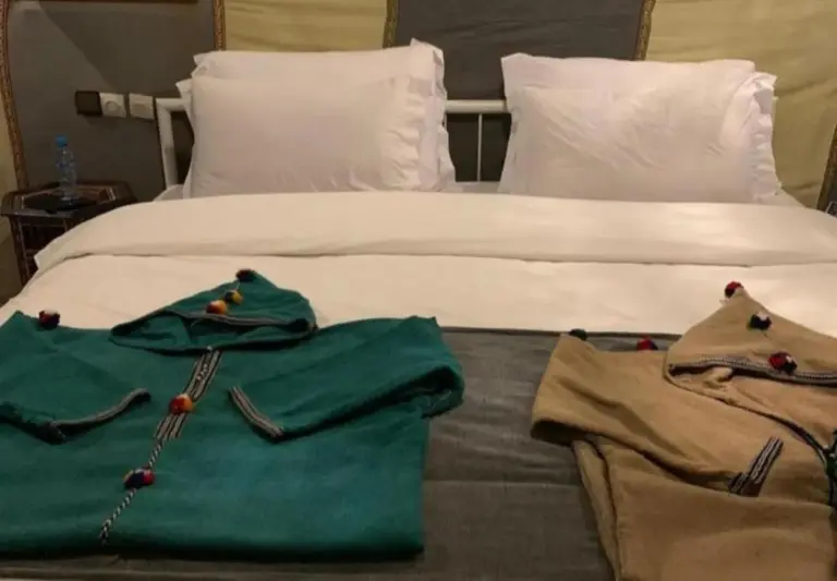 Guest bed at Merzouga Retreat Camp in Merzouga with folded robes placed on top of a neatly made bed.