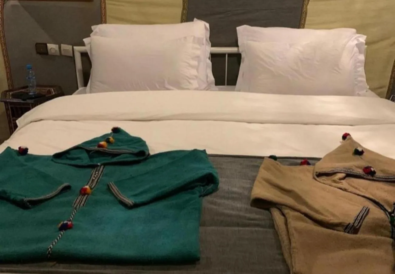 Guest bed at Merzouga Retreat Camp in Merzouga with folded robes placed on top of a neatly made bed.