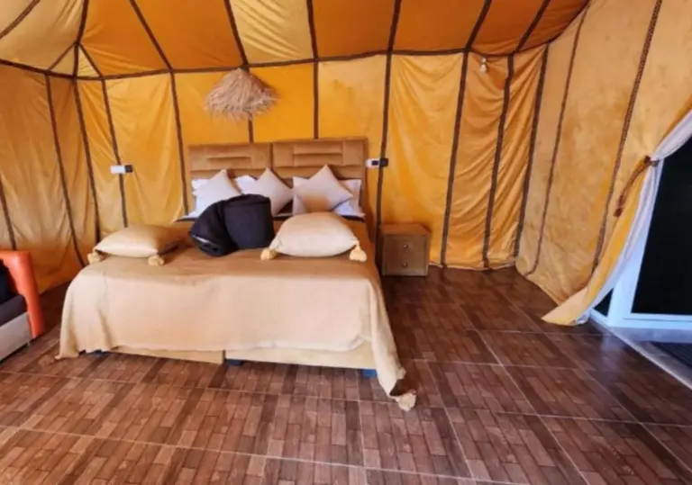 A tent bedroom at Merzouga Retreat Camp in Merzouga with a double bed, pillows, and wood-look flooring.