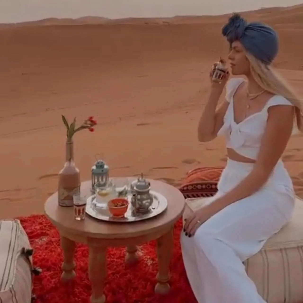 Mujer bebiendo té en el desierto en Merzouga Royal Camp en Merzouga con una mesa baja y dunas al fondo