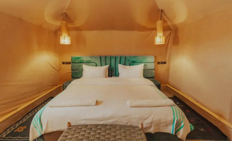 Amplia habitación tienda de lujo en Merzouga Royal Camp en Merzouga con una cama grande y un diseño interior cálido