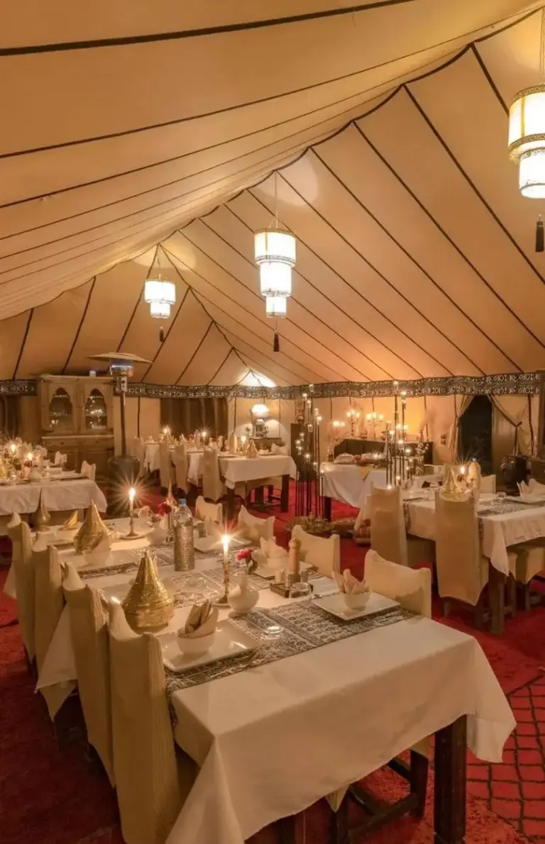 Elegantes Speisezelt im Merzouga Sara Luxury Camp in Merzouga mit gedeckten Tischen und Laternenbeleuchtung