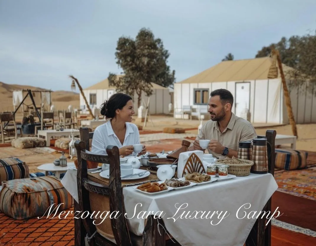 Frühstück im Freien im Merzouga Sara Luxury Camp in Merzouga mit Gästen, die im Innenhof des Wüstencamps speisen