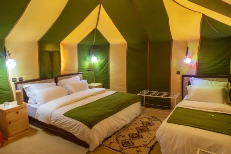 Zweibett-Zeltzimmer im Milky Way Desert Camp in Merzouga mit zwei Betten, grünen Akzenten und warmer Beleuchtung des Wüstencamps