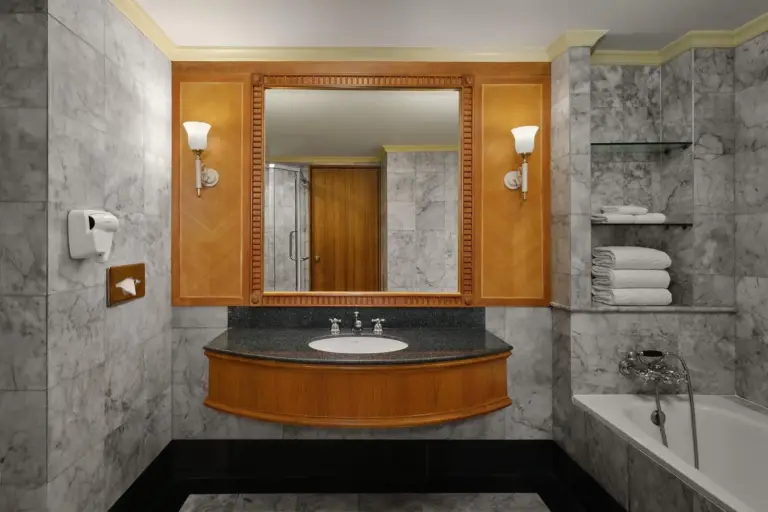 Bathroom at Montien Riverside Hotel Bangkok with marble walls, vanity mirror, bathtub, and built-in shelving.