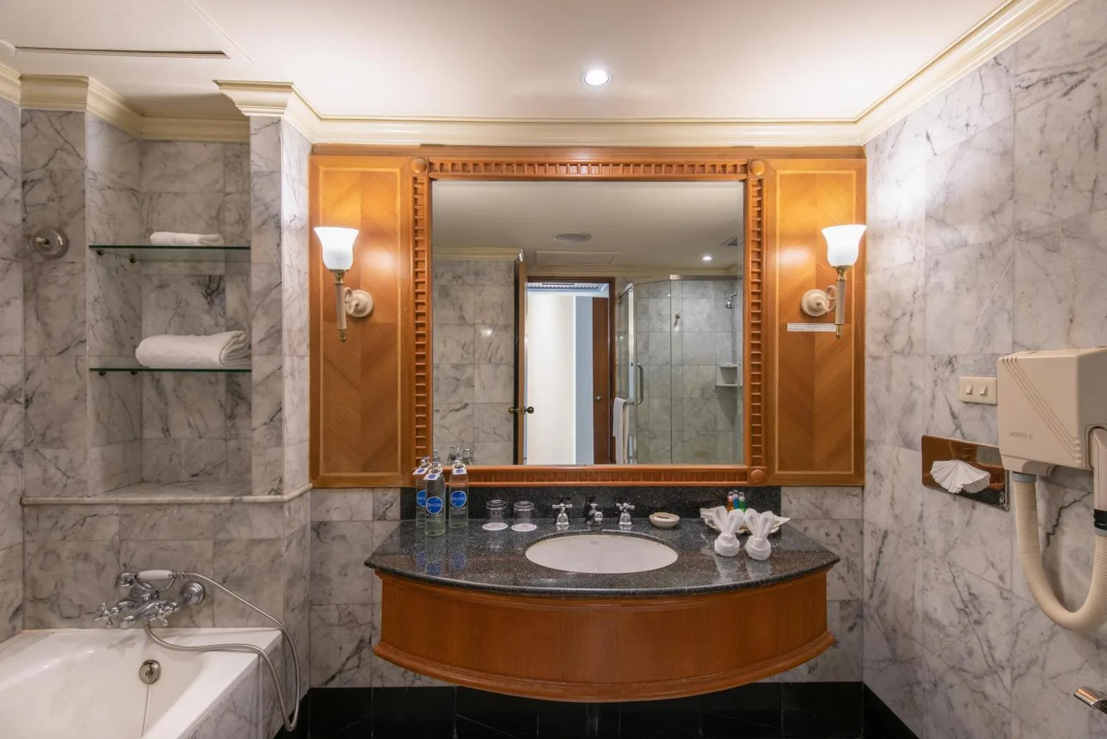 Bathroom vanity at Montien Riverside Hotel Bangkok with marble countertop, large mirror, bathtub, and toiletries.