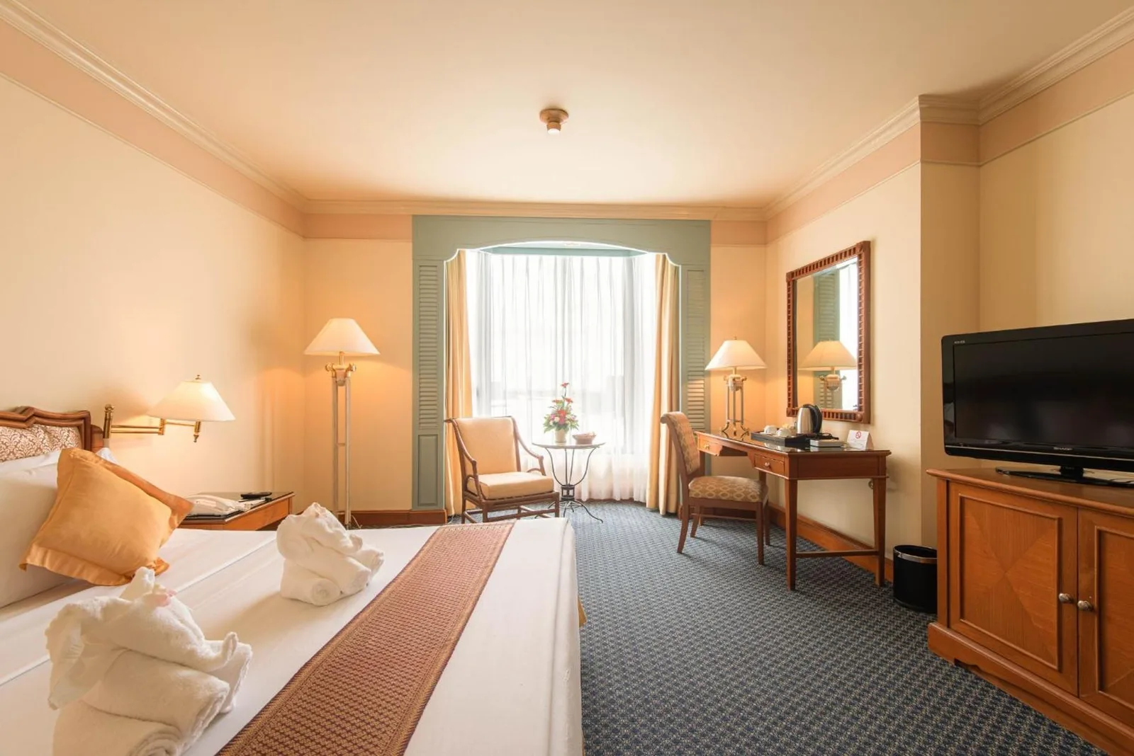 Spacious guest room at Montien Riverside Hotel Bangkok with a king bed, seating area, desk, and large window.